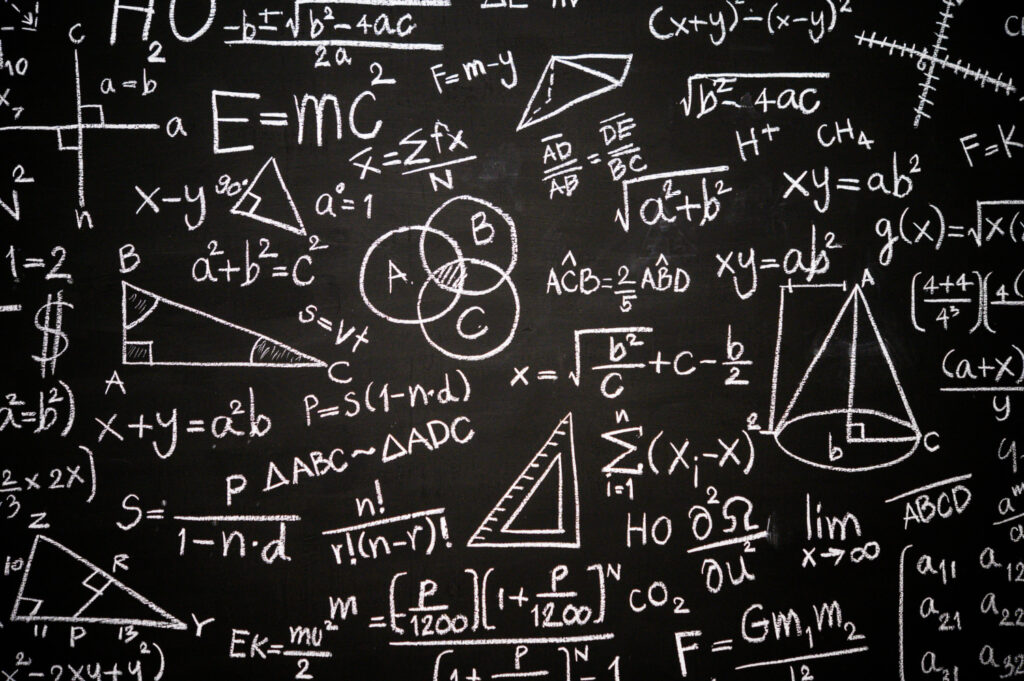 Czarna tablica szkolna zapisana białymi wzorami matematycznymi, równaniami i figurami geometrycznymi, jak gry matematyczne.